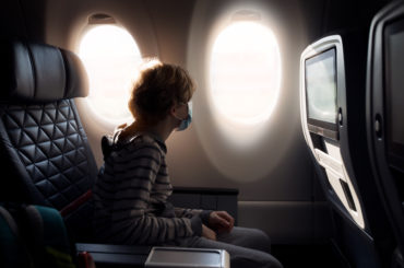 boy wearing face mask sitting in airplane cabin